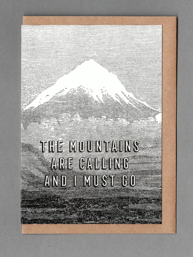 Black and white card with a mountain on it and text reading 'THE MOUNTAINS ARE CALLING AND I MUST GO' with brown envelope behind it