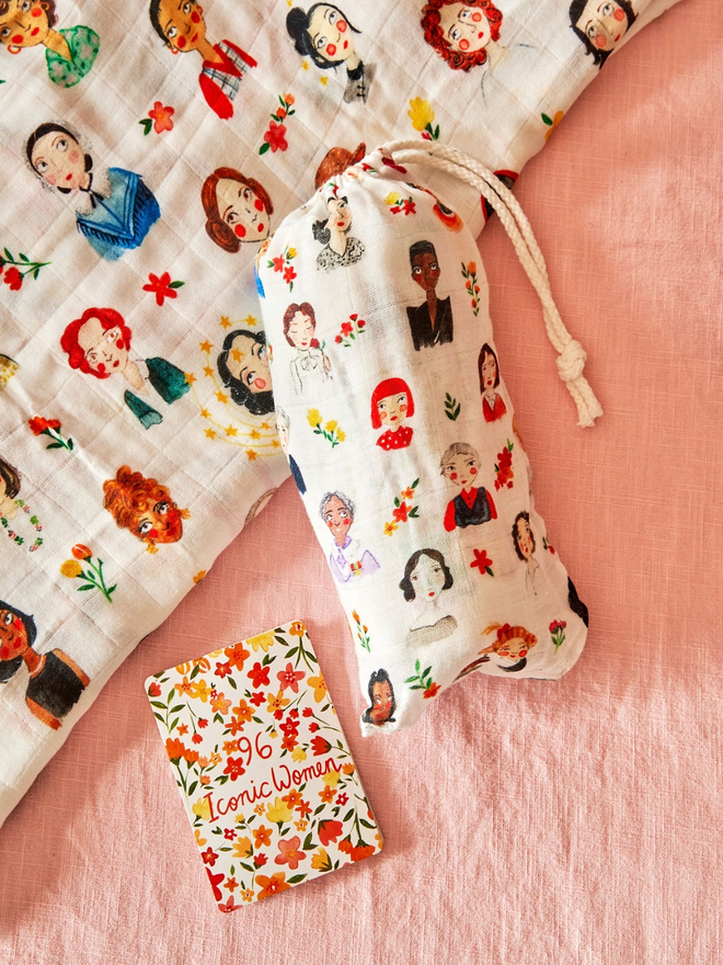 The iconic women swaddle blanket packaged in drawstring bag alongside fold out guide naming 96 inspiring women featured on the blanket