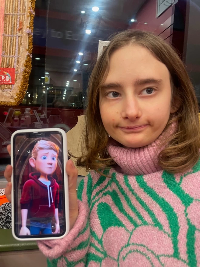 Piper holding up her phone that has an animated photo of her imaginary boyfriend. he looks worried and she looks proud