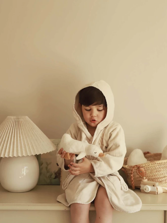 Boy wearing a towelling robe cuddling a plush duck