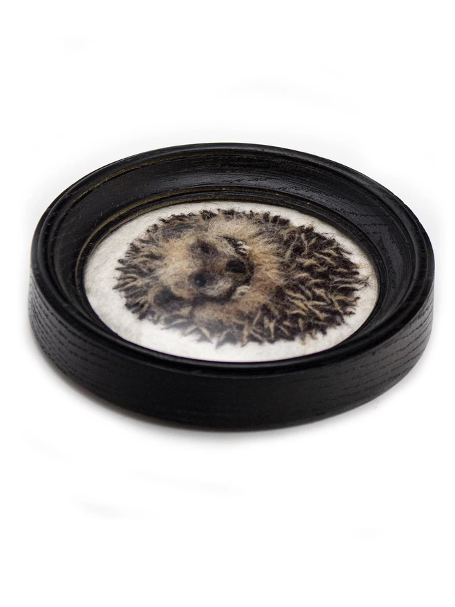 A needle-felted hedgehog picture in a round black frame