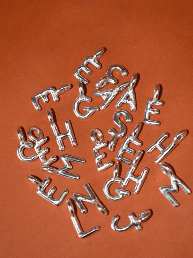 an assortment of silver alphabet/initial pendants lay scattered on an orange background