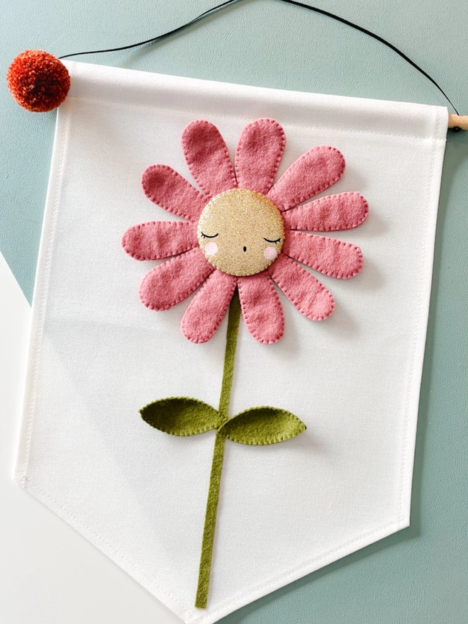 A pink Daisy with a gold face on a white banner