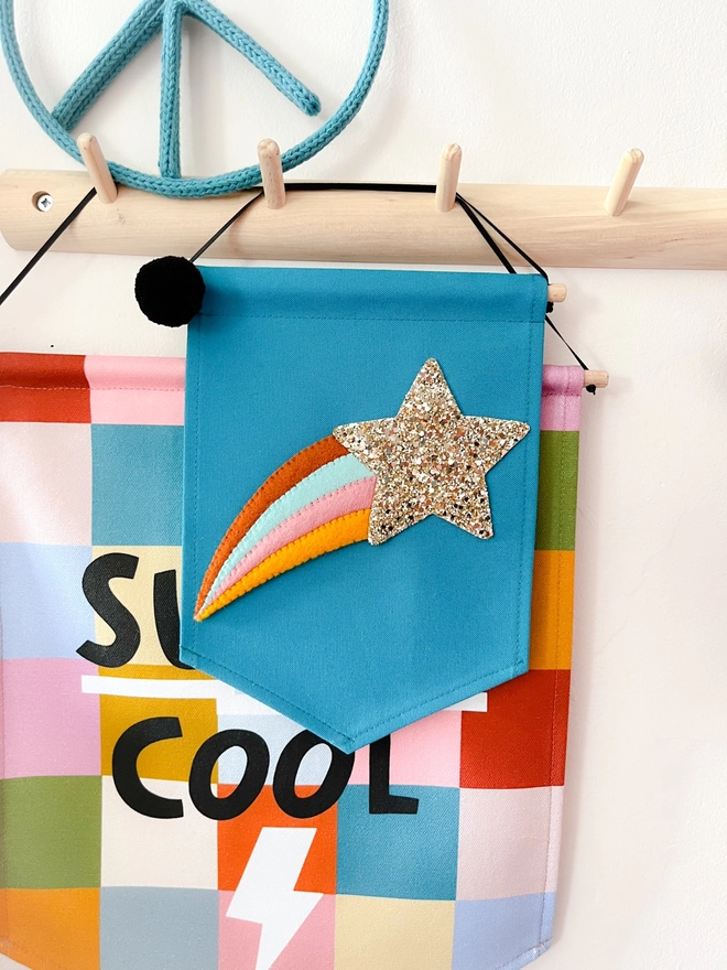 Teal coloured shooting star banner hanging from a wooden peg rail