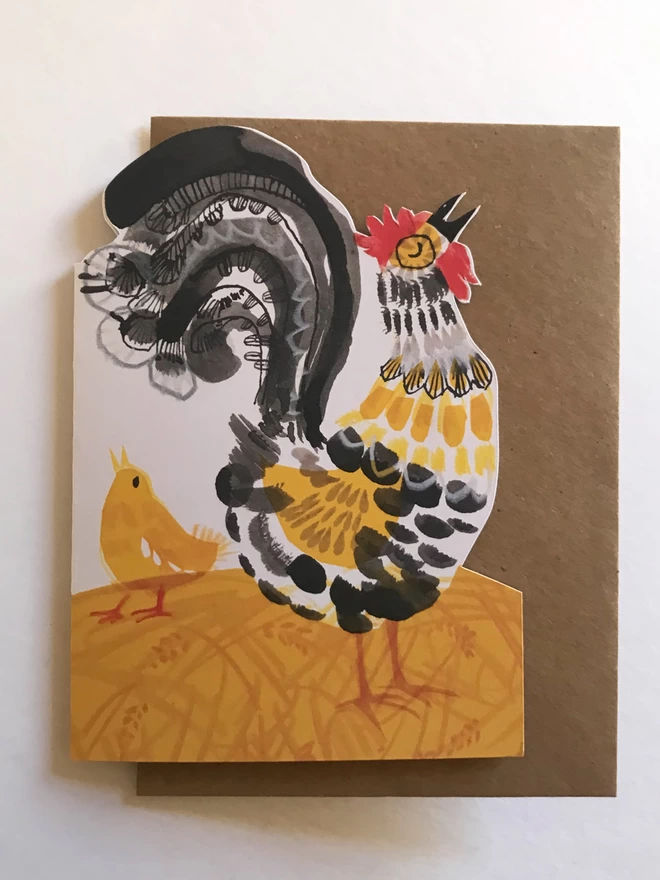 Shaped Crowing Cockerel greetings card illustrated by Esther Kent in in yellow and black, stands against a white background