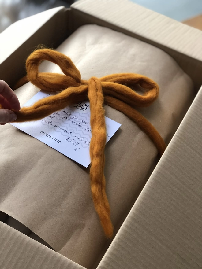 A cardboard box, with a Mizzknits gift card and a large woolly amber bow