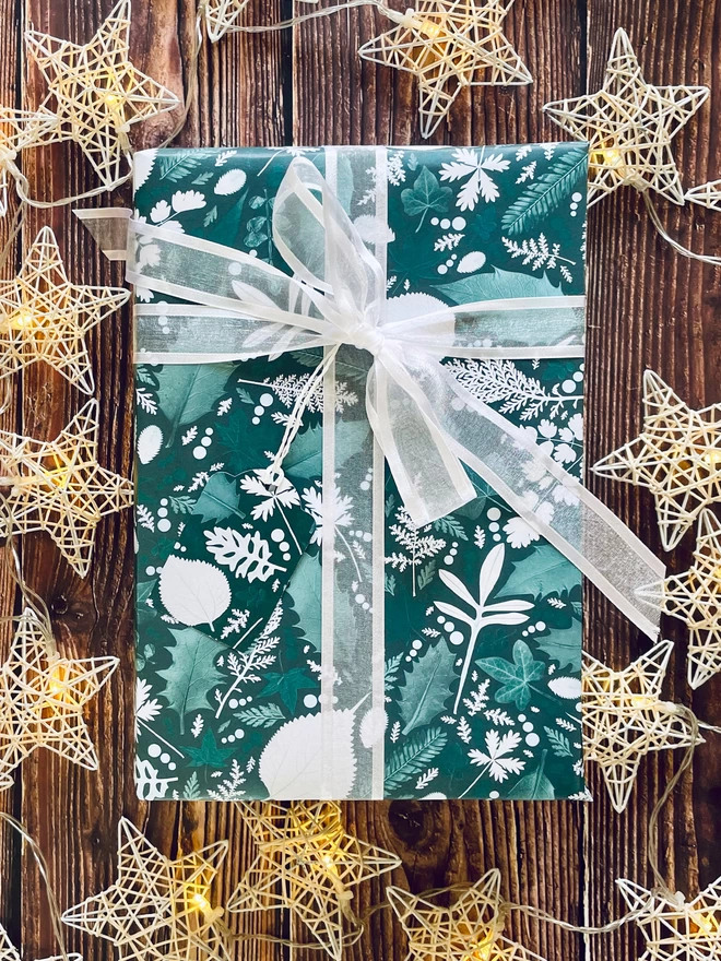 Present wrapped in festive green and white pressed leaf print wrapping paper with Holly and Ivy design. “Recycled and recyclable