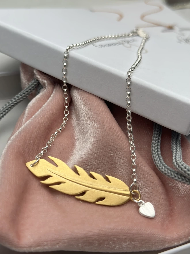 sterling silver chain with gold horizontal feather charm. a small silver heart charm hangs from the chain next to the feather