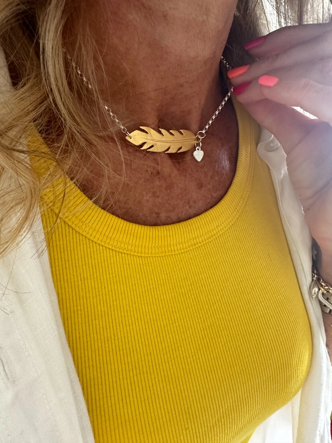 model wears a gold plate feather charm on a sterling silver chain with additional silver mini heart