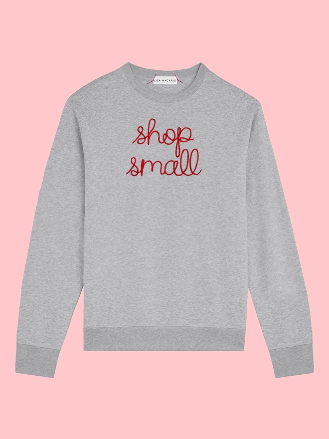 A grey sweatshirt embroidered with shop small on a pink background