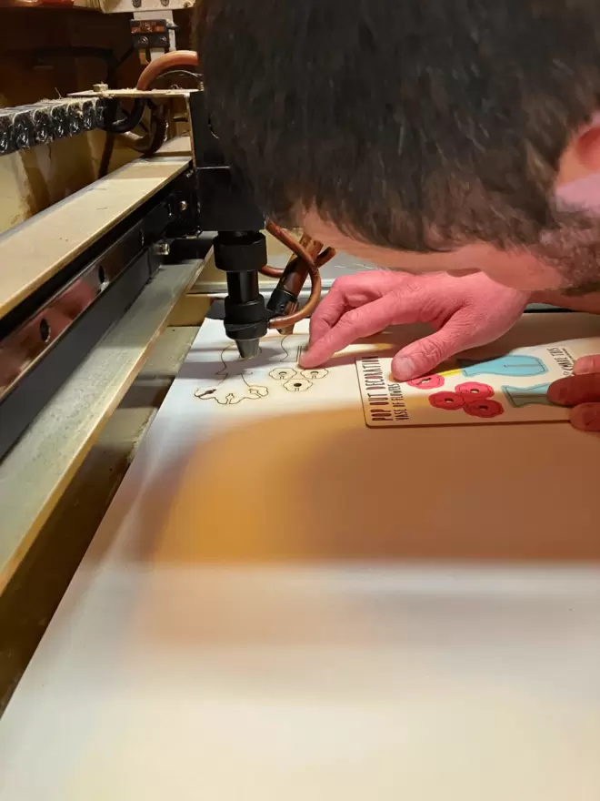 A man operating a laser cutting machine looking at the flower decorations that he has laser cut