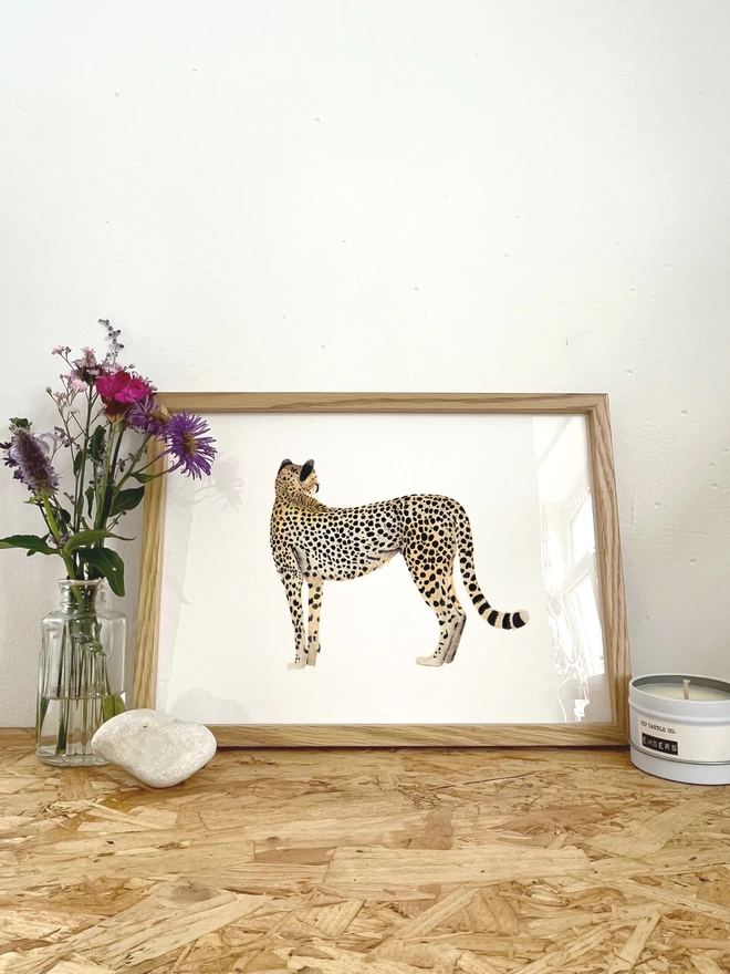 a print of an illustration of a cheetah looking away in a frame next to some flowers 
