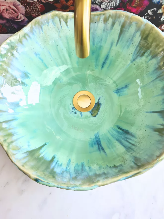 Handcrafted ceramic bathroom basin in a turquoise green blue glaze, hand-crafted sink, pottery basin, wc, bathroom, ensuite, modern bathroom, photographed against colourful floral wallpaper with gold taps, homeware, interiors, close up