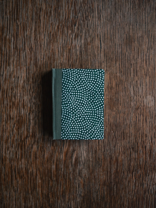 Miniature book with a green cover with white dots and green cloth spine
