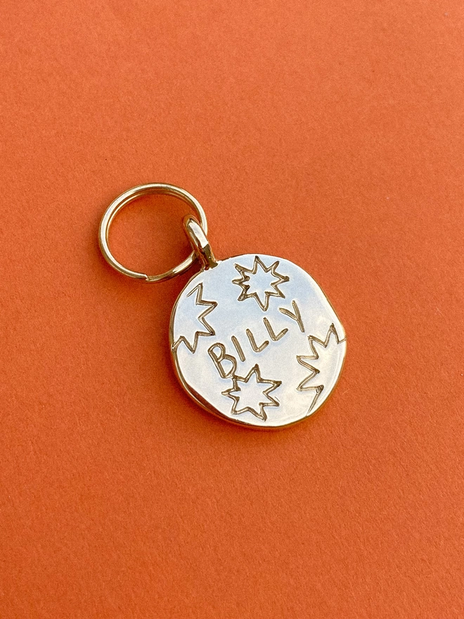 a round pet tag in shiny brass, hand engraved into the tag is 'BILLY' surrounded by stars.