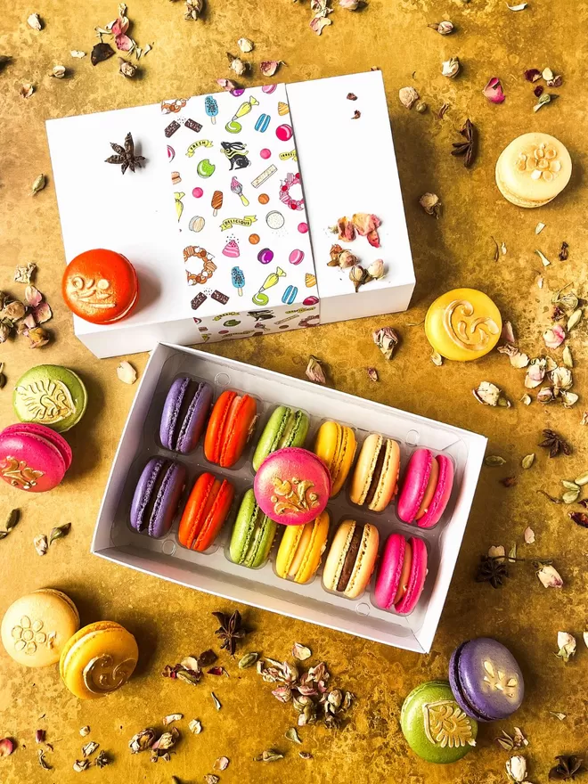 colourful Diwali themed macarons with gold henna designs in a white box on a gold background with rose petals