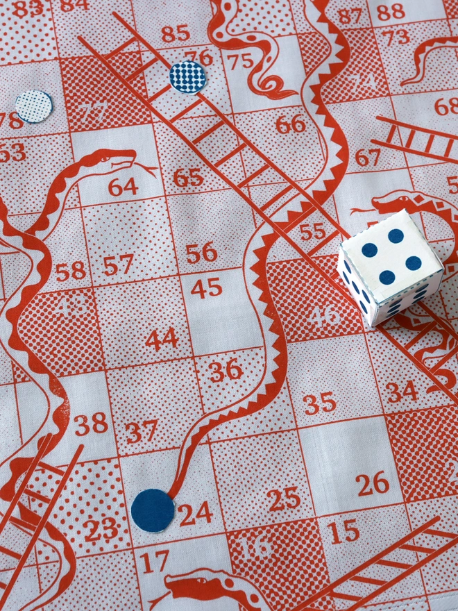 a detail of an orange snakes & ladders hankie with die and counters on the game board.