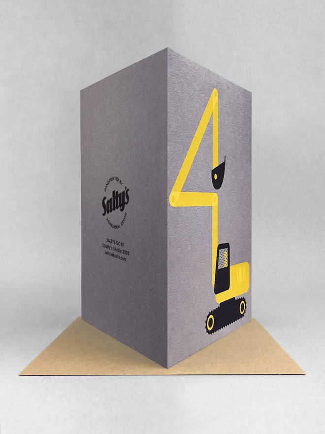 Rear view of a yellow and black digger, with its arm bent into a number 4 shape - screenprinted onto a grey card. Its is stood on a brown kraft envelope in a light grey studio with soft shadows.