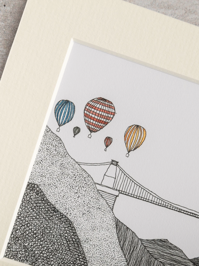 Print of detailed pen and watercolour drawing of air balloons above Clifton Suspension Bridge, in a soft white mount