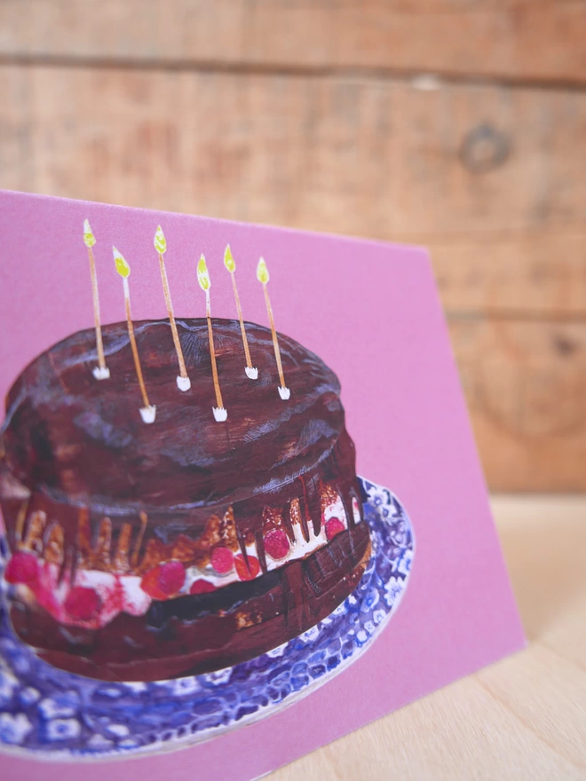 A close up of the illustration of the chocolate & raspberry birthday cake on its pink background. 