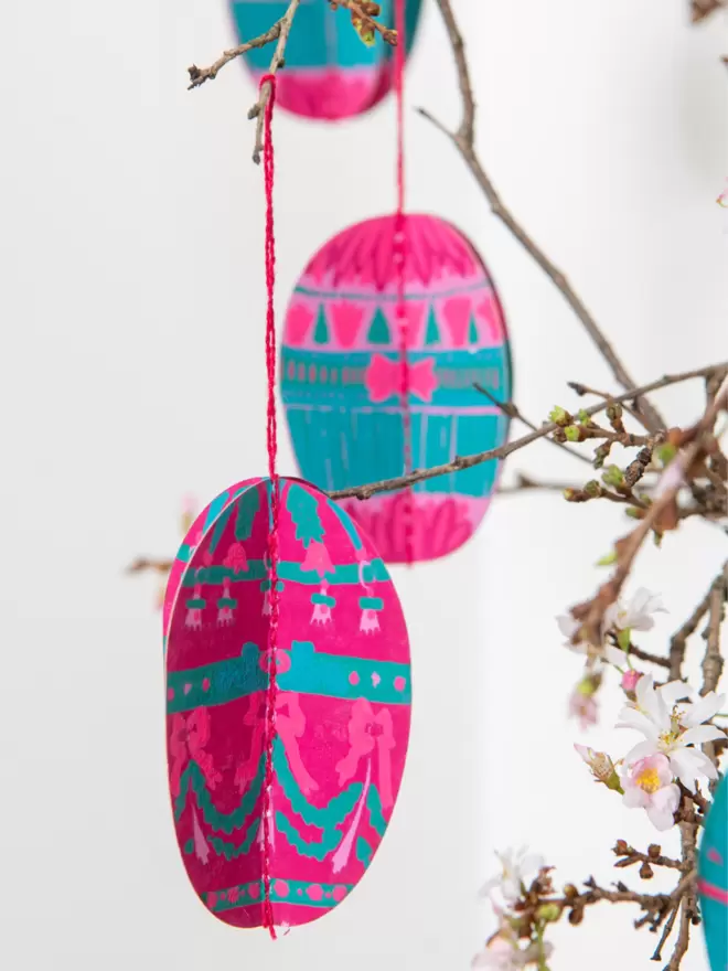 Close-up, detailed shot: pink and blue detailed paper eggs hanging on branch