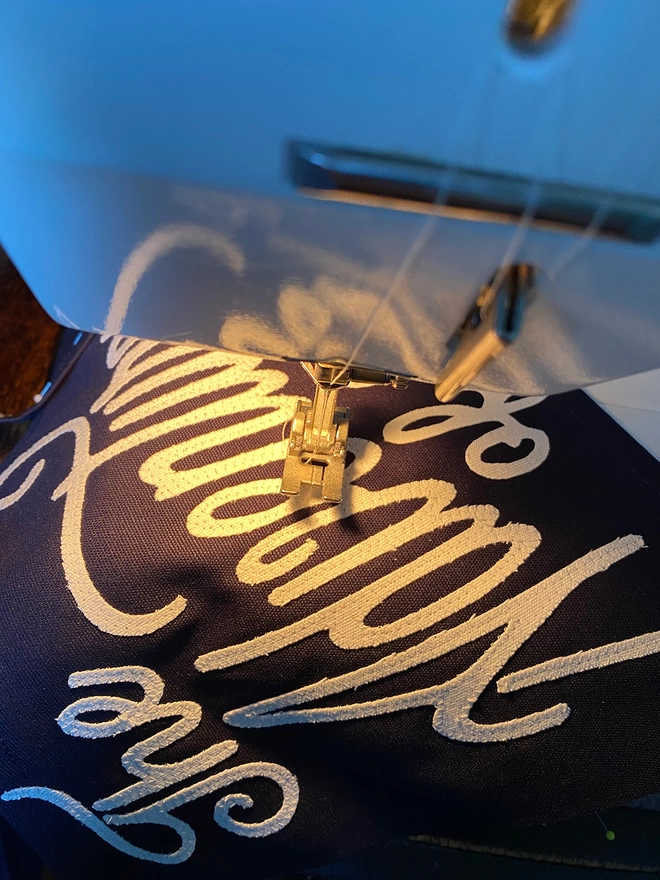 A photo showing the word adventure being sewn onto a pennant flag