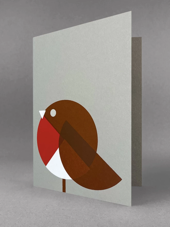 Geometric shapes in red white and brown make up this handprinted robin christmas card, stood slightly open, in a light grey set.
