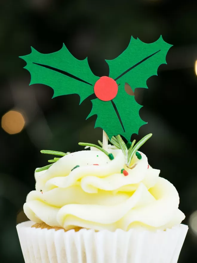 Closeup of Christmas cupcake topper.  Paper decoration features three leaved holly sprig with a central red berry