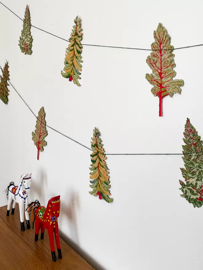 Forest garland hanging on white wall - white and red wooden horses in foreground