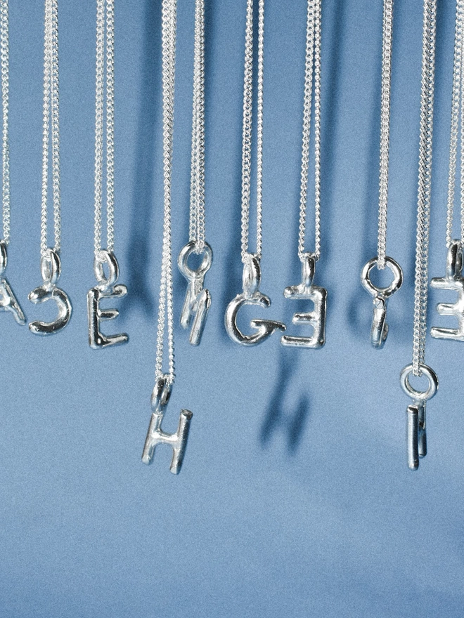 silver wobbly alphabet letter pendants hang on thin silver chains in varying lengths.