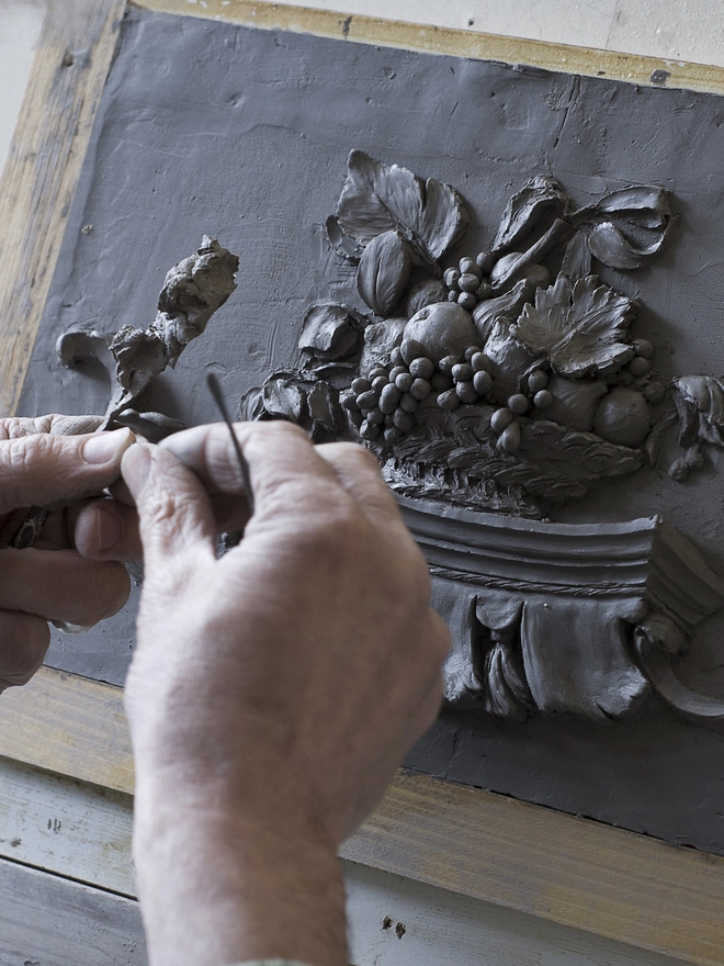 Sculptor modelling Still Life relief plaque in clay with hands and modelling tools