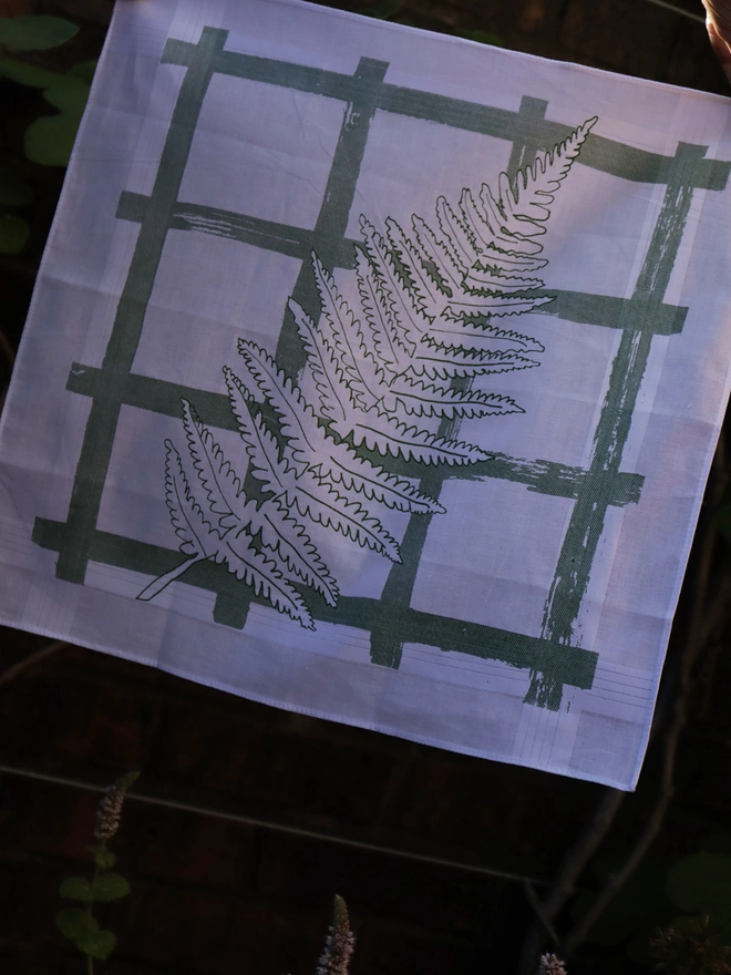 A Mr.PS Flourish fern leaf print handkerchief held against a garden wall
