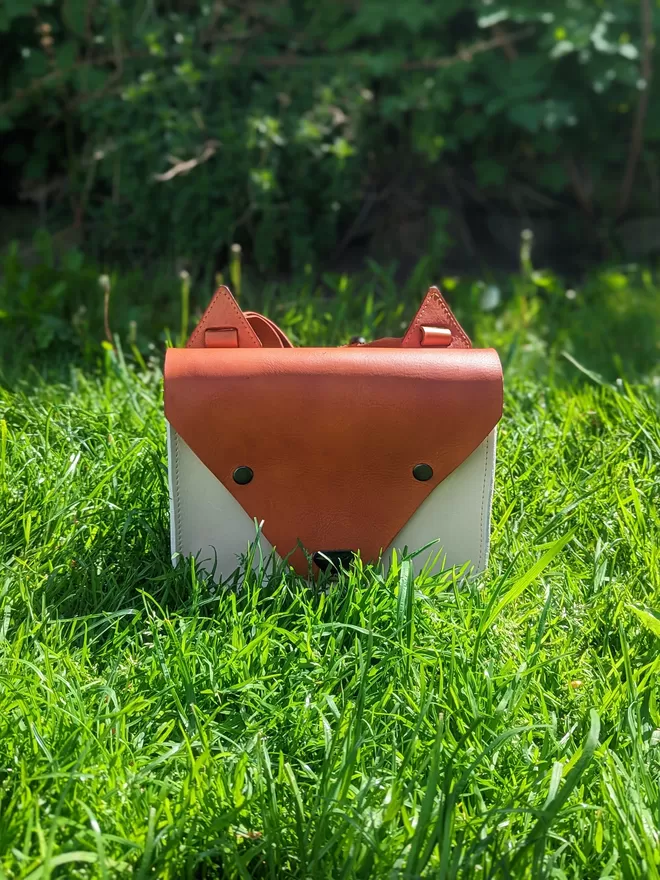 hand-dyed orange and light tan leather fox backpack on grass.