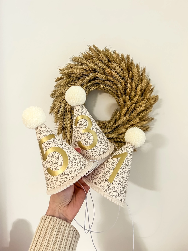 Natural Floral Party Hats with Gold Numbers and Cream Pom Poms in front of a Wheat Wreath