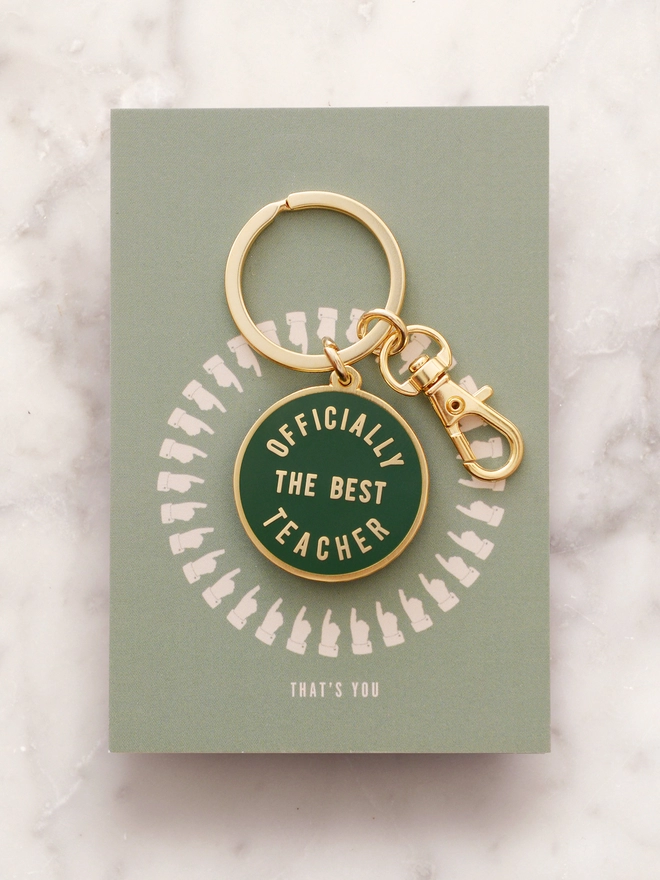 green keyring with 'officially the best teacher' design laying on marble