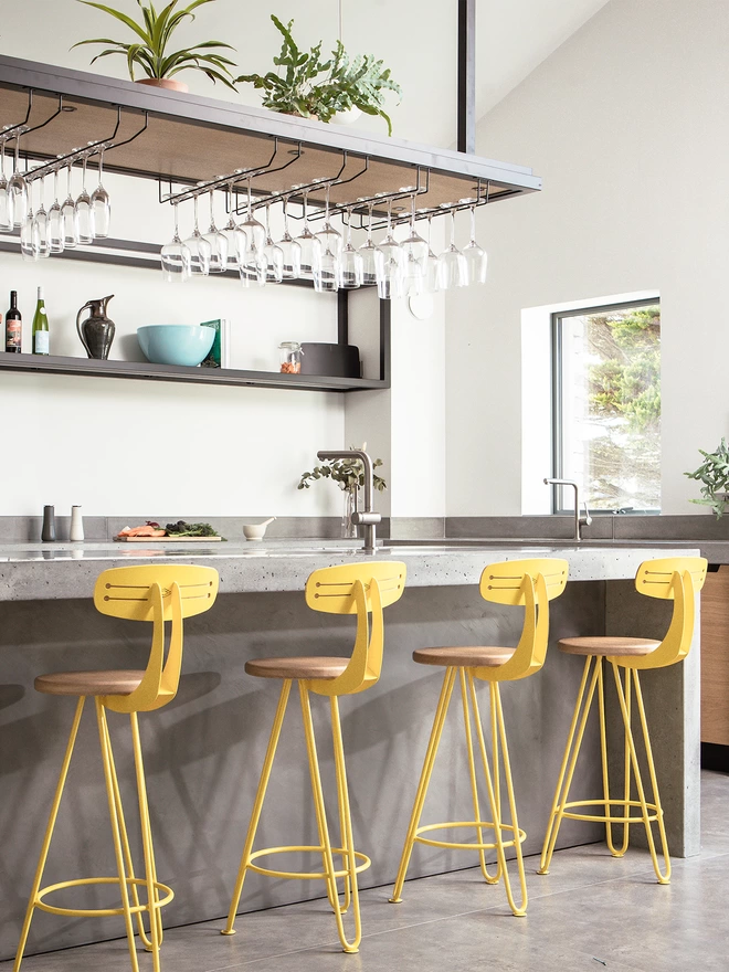 set of four bright yellow hairpin leg bar chairs with oak seats, pushed up against a polished concrete kitchen island