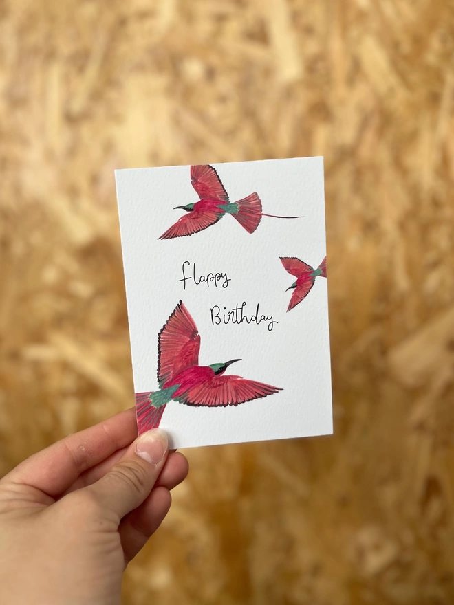 a greetings card featuring three pink carmine bee-eater birds with the phrase “flappy birthday”
