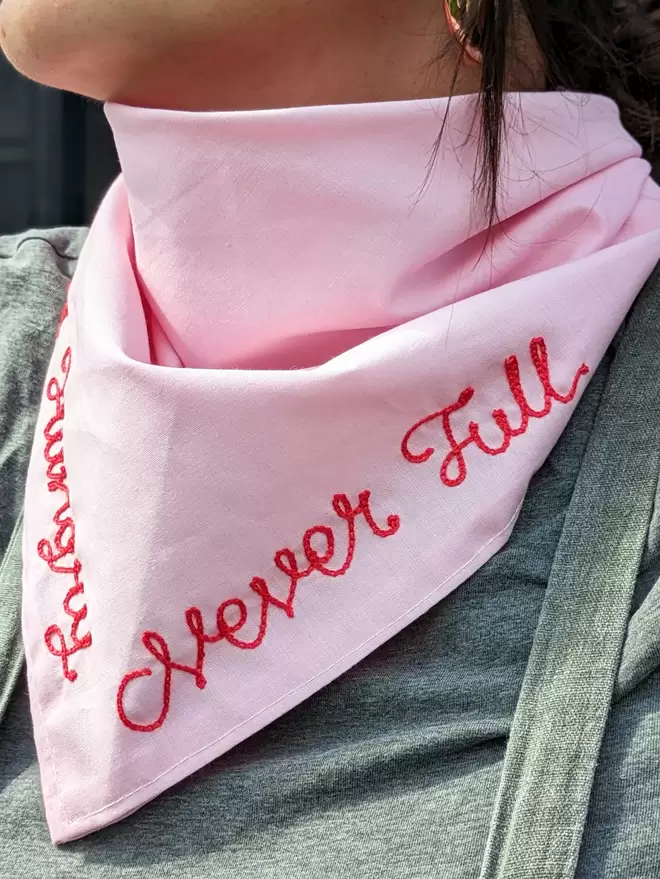 Woman wearing a pink Bandana Neckerchief with White Embroidered lettering readiing "Always Hungry, Never Full"