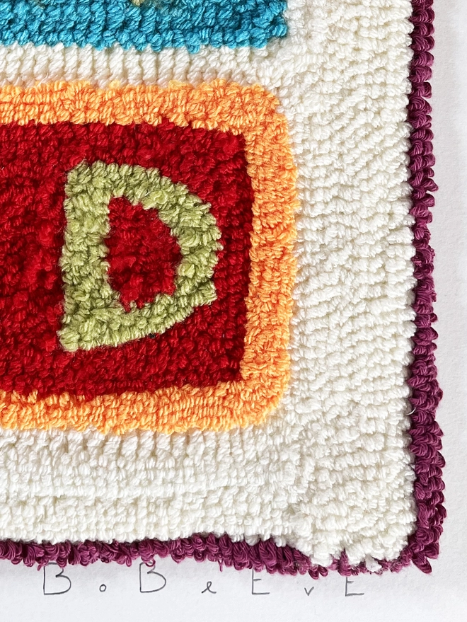 Punch needle lime green "D" on red wool block with orange edging