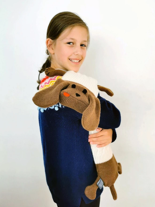 A smiling girl cuddles Dolly the Sausage Dog hot water bottle.t