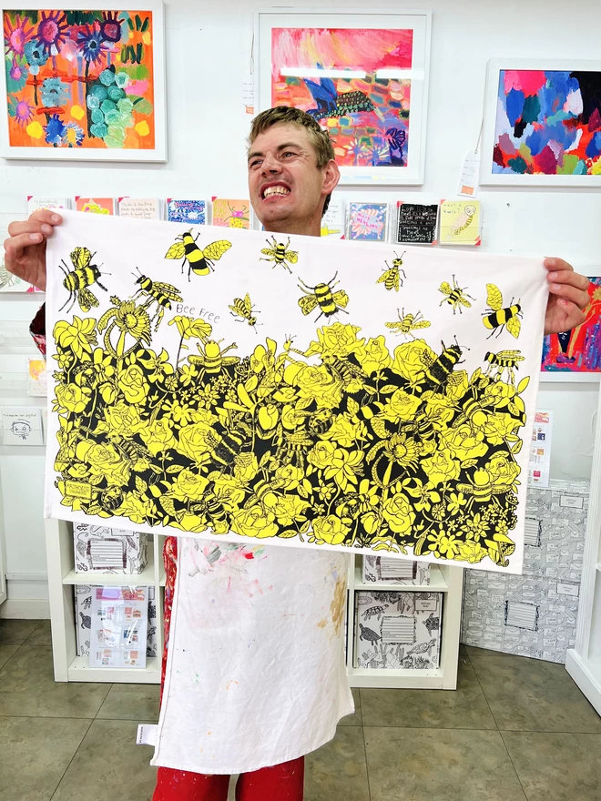 Smiling artist holding bee free 100% organic cotton charity tea towel in arthouse unlimited studio 