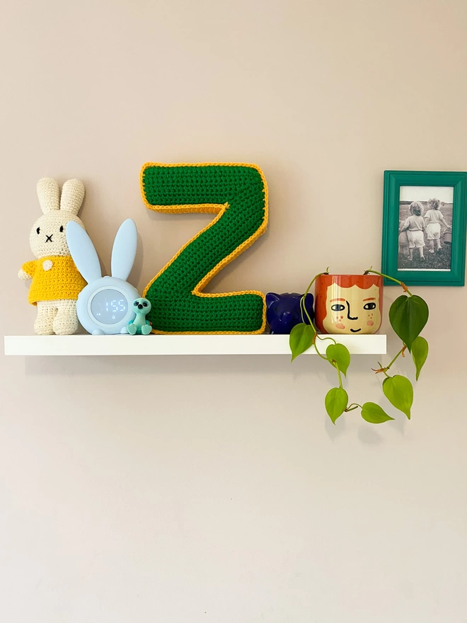 Crochet cushion shaped like a Z in Grass Green and Pale Orange, on a shelf
