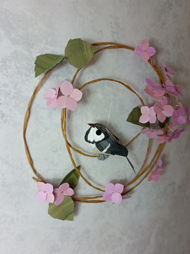 Coal tit sculpture, perched on a wreath of pink hydrangea blossoms.