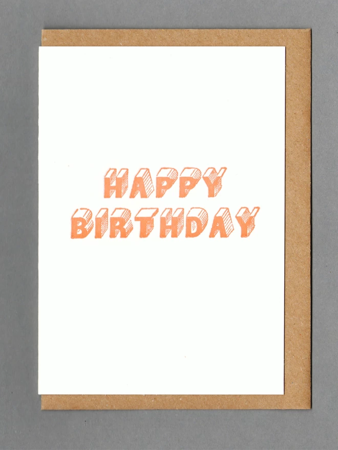 White card with orange text reading 'Happy Birthday' with a brown envelope behind it