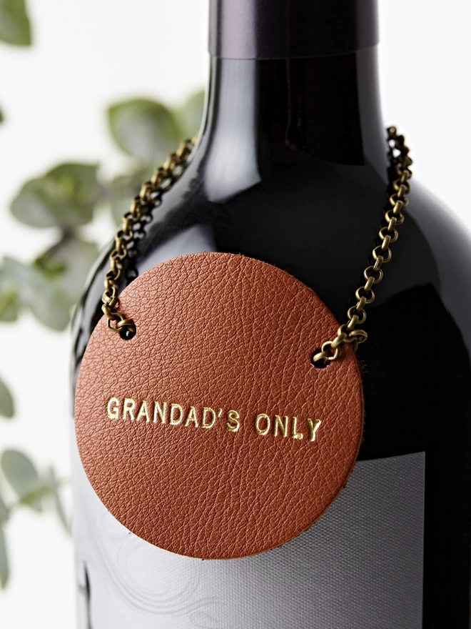 Tan leather bottle tag on a bottle of wine. 'Grandad's Only'