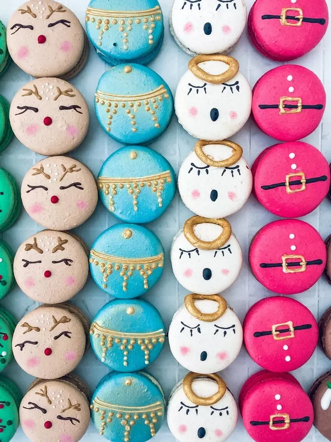 several decorated macarons themed like Christmas character - fairy lights, rudolf the red nosed reindeer, Christmas bauble, angel, Santa and Christmas pudding are arranged on a table