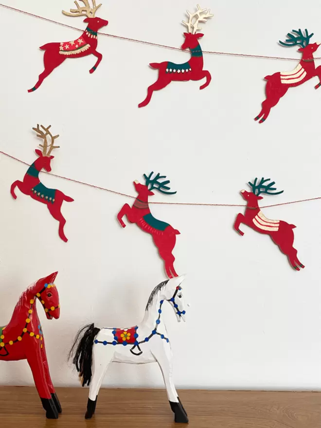 Pink and teal reindeer shapes hung on white background with red and white horse wooden statues in foreground