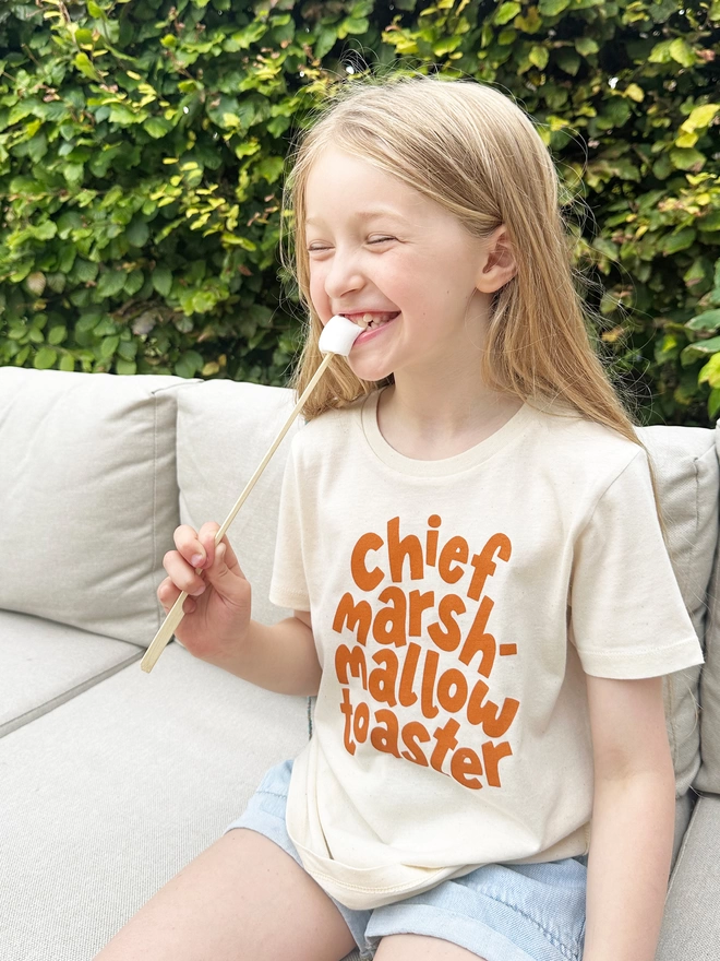 girl wearing a chief marshmallow toaster organic cotton t-shirt whilst eating a toasted marshmallow 