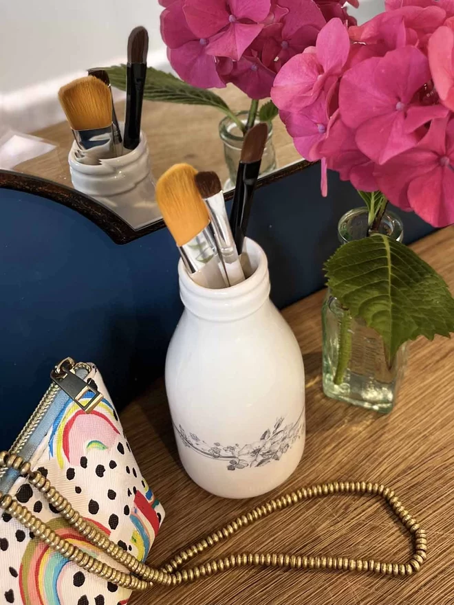 A small handmade ceramic ‘milk’ bottle is holding a selection of makeup brushes. 