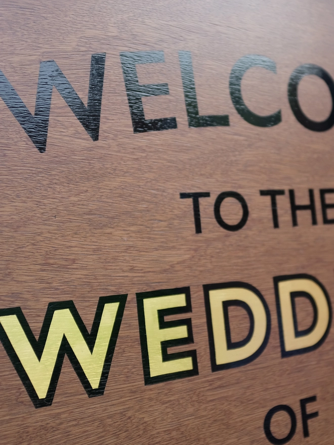 Close up of welcome to the wedding sign showing the glossiness of the black letters